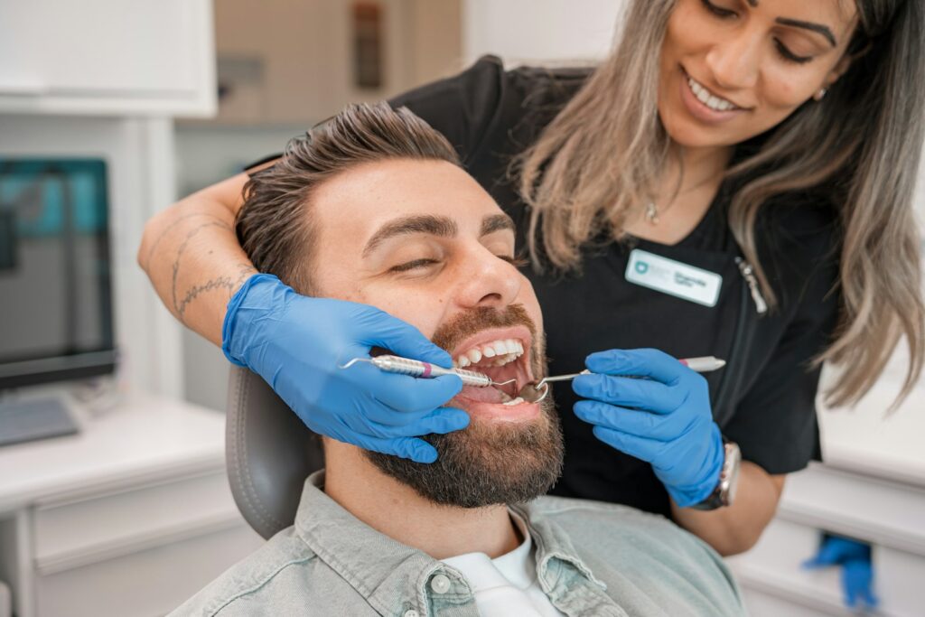 Dentist in blue gloves examining a man's teeth during a check-up in a dental office